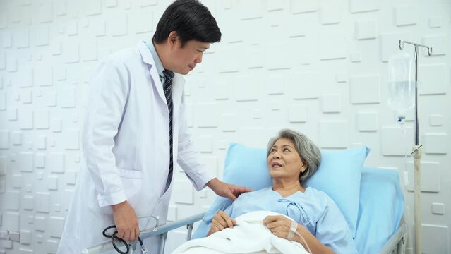 Male doctor came to inquire about the symptoms of an elderly female patient lying in bed receiving saline in the patient's room. Elderly female patient responds Male doctor with a smiling face.