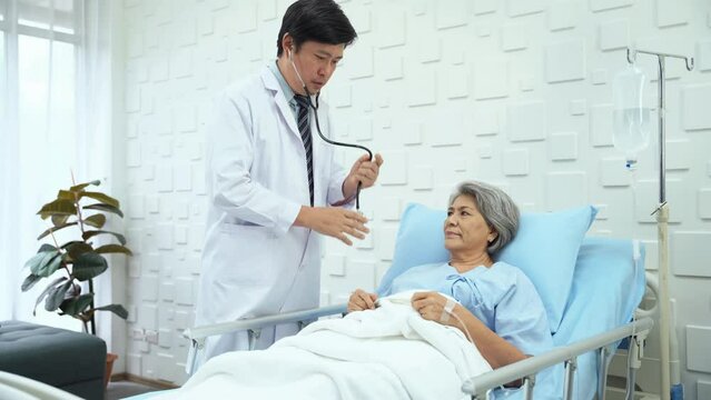 Specialist male doctor to check the symptoms of elderly female patient saline bed in bed in patient room. Male doctor using a stethoscope Examine the lungs, heart sounds, and other organ sounds.