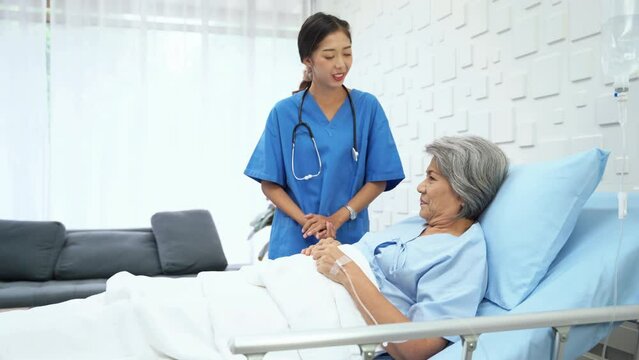 Expert female doctor Asked about the symptoms of an elderly woman lying in bed receiving saline in the patient room. An elderly female patient responds to a female doctor with a smiling face.