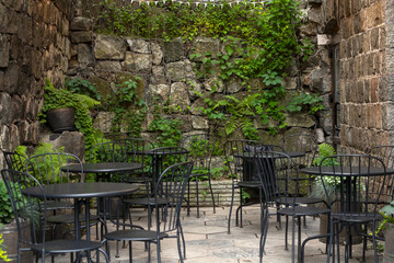 Fototapeta na wymiar Atmospheric summer photography. Outdoor cafe with black chairs and tables. Outdoor street cafe with lots of plants
