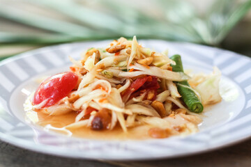 Thai papaya salad on a plate, papaya salad with poop, lemon, pepper, red tomato in white bowl on wooden table