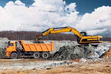 A powerful crawler excavator loads the earth into a dump truck against the blue sky. Development and removal of soil from the construction site.