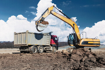 A powerful crawler excavator loads the earth into a dump truck against the blue sky. Development...