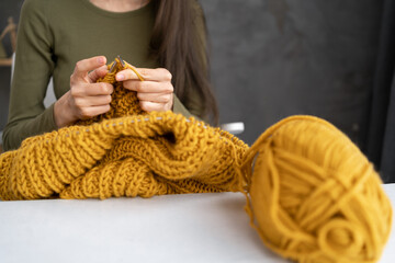 Close-up of female hands knitting wool sweater. Woman knits from thick yarn. Handmade clothes. The girl goes in for her hobbies. Knitting