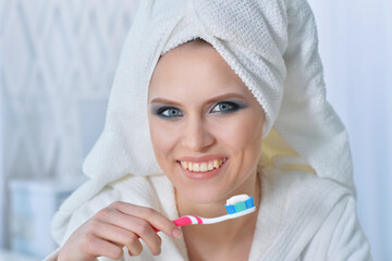 Beautiful girl in a bathrobe brushing her teeth