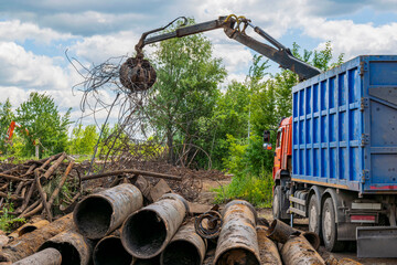 Scrap metal waste (steel and cast iron pipes) is loaded into truck using hydraulic manipulator with grab.