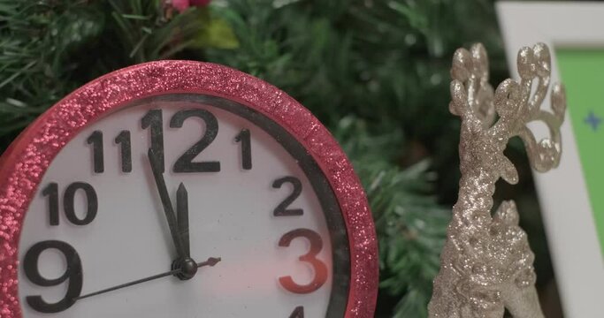 Pink shiny clocks, silver christmas deer toys and photo frame mockups in front of christmas tree branches, close up