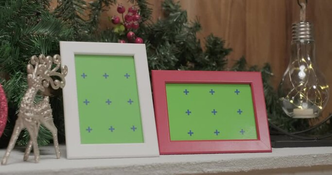 Pink shiny clocks, silver christmas deer toys and photo frame mockups in front of christmas tree branches, close up