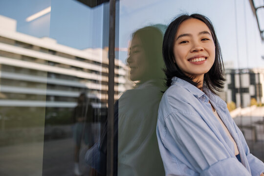 Side view of cute pretty asian woman look with smile at camera .Wearing blue shirt staying near to wall with cooy space for your advertising. Lifestyle, street style concept 