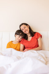 Fototapeta premium A child with mom sit on the bed, a woman hugs her son
