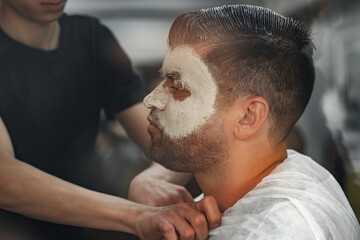 Relaxed man having purifying mask on face in a barbershop