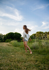 free slim brunette woman walking on the meadow opposite blue sky
