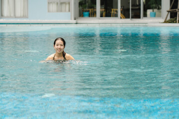 A cute teenage Asian female tourist is happily swimming in the pool on a day of sightseeing and relaxing at the hotel. A woman swims happily and happily in the pool alone on a clear day.