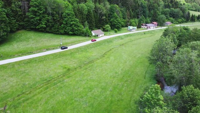 Two cars on a rural mountain road surrounded by green fields and forest in Vosges, France 4K