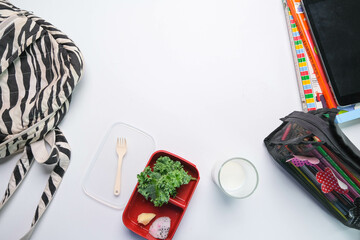 Healthy lunch box with vegetables, fruit and milk in glass on the school table. Lunch boxes, bags and stationery on the table.