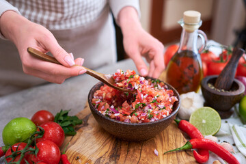 making salsa dip sauce - woman mixing chopped ingredients in wooden bowl