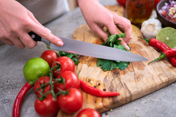 making salsa dip sauce - woman cutting and chopping cilantro or parsley on wooden cutting board