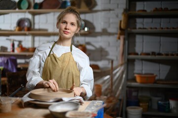 A ceramist makes a plate. Woman in an apron works in a pottery workshop. 