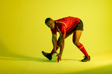 Fototapeta na wymiar African american male rugby player with rugby ball over yellow lighting