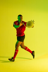 Fototapeta na wymiar African american male rugby player catching rugby ball over yellow lighting