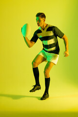 Caucasian male rugby player with rugby ball over yellow lighting