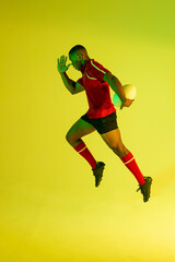 Fototapeta na wymiar African american male rugby player running with rugby ball over yellow lighting