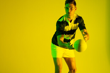 Caucasian male rugby player catching rugby ball over yellow lighting