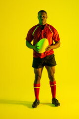 Fototapeta na wymiar Portrait of african american male rugby player with rugby ball over yellow lighting