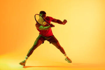 Fototapeta na wymiar Image of african american male tennis player hitting ball in yellow lighting