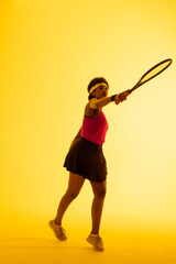 Fototapeta na wymiar Vertical image of african american female tennis player hitting ball in yellow lighting
