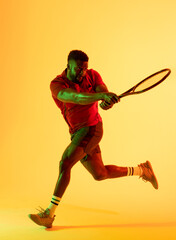 Fototapeta na wymiar Vertical image of african american male tennis player hitting ball in yellow lighting