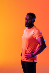 Vertical image of african american male athlete looking at camera in neon orange lighting