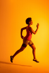 Vertical image of african american female athlete running in neon orange lighting