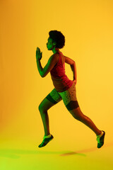 Fototapeta na wymiar Vertical image of african american female athlete running in yellow lighting