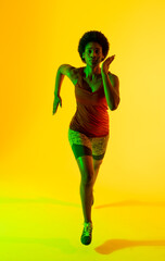Vertical image of african american female athlete running in yellow lighting