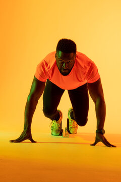 Vertical image of african american male athlete preparing for run in yellow lighting