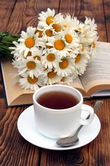 Still life with a cup of tea with a bouquet of daisies on the table.