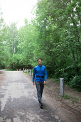 Sporty man in blue sportswear walking on the road close to the forest after jogging