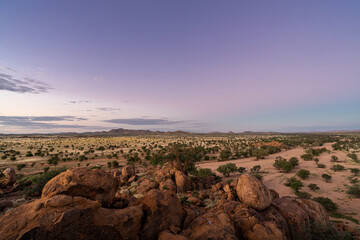 Fototapeta na wymiar A beautyful Sunset with violet colors in the sky and boulders in the foreground. View of the surrounding desert in Namibia, during the rainy season. Lots of green vegetation.
