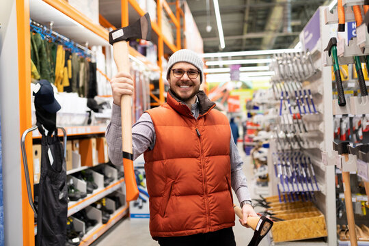 a man in a construction hypermarket chose an ax for cutting trees