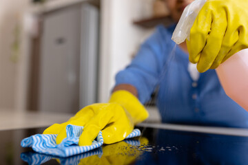 Midsection of biracial mature woman spraying disinfection on kitchen counter and cleaning with rag