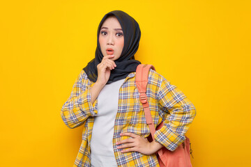 Pensive young Asian Muslim woman student in casual clothes and backpack, looks seriously thinking about a question isolated on yellow background. Education school university college concept