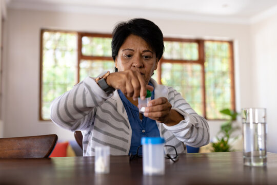 Biracial mature woman with short hair taking medicines while sitting at wooden table at home