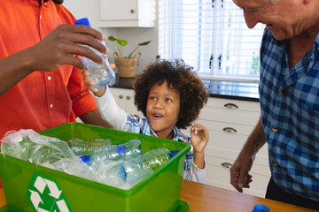 Multiracial father and grandfather teaching boy to recycle waste by throwing plastic bottles in bin
