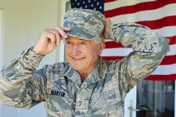 Smiling caucasian senior army soldier in camouflage clothing wearing cap against flag of america