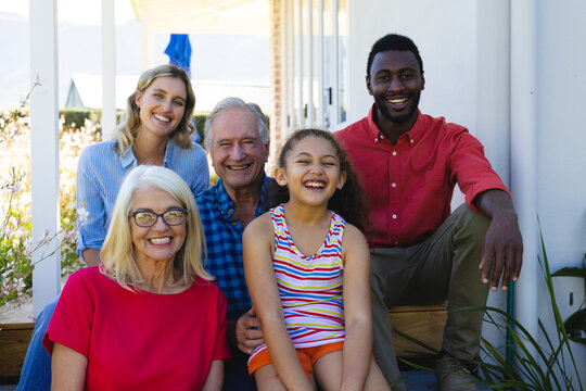 Portrait of cheerful multiracial multigeneration family sitting outside house in yard