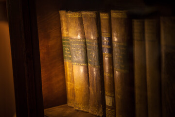 Antique antique books are piled on a wooden surface in a warm directional light. Selective focus.