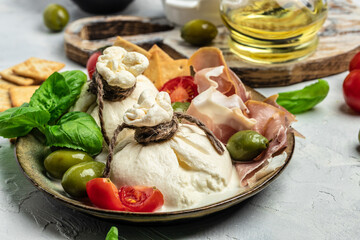 Italian tomatoes and burrata cheese salad served with cherry tomatoes, fresh basil leaves, prosciutto ham and olives on a light background. Restaurant menu top view