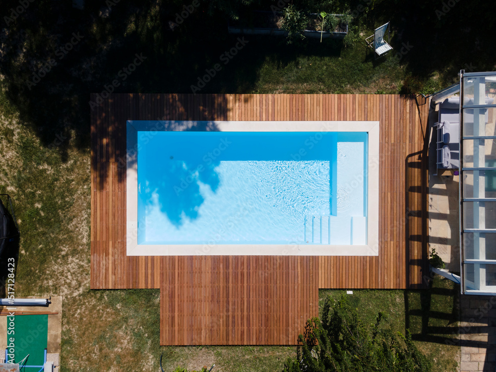 Wall mural Drone flight over pool with nice wooden terrace surrounded by green lawn in beautiful garden