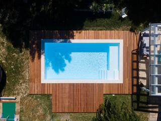 Drone flight over pool with nice wooden terrace surrounded by green lawn in beautiful garden